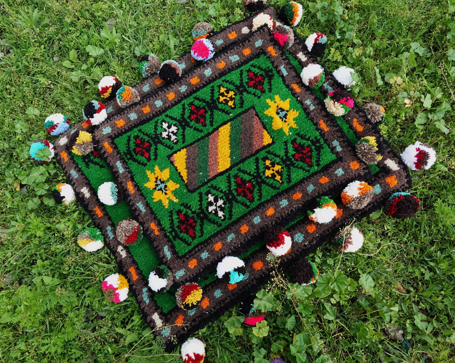Close view of green woven Shabrak with striped centre panel and pompom border