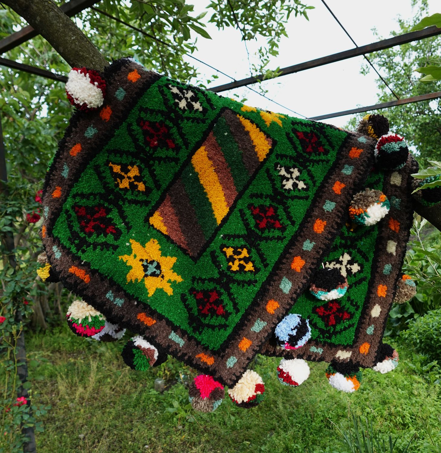 Green woven Shabrak hanging from a branch with orange and brown geometric pattern