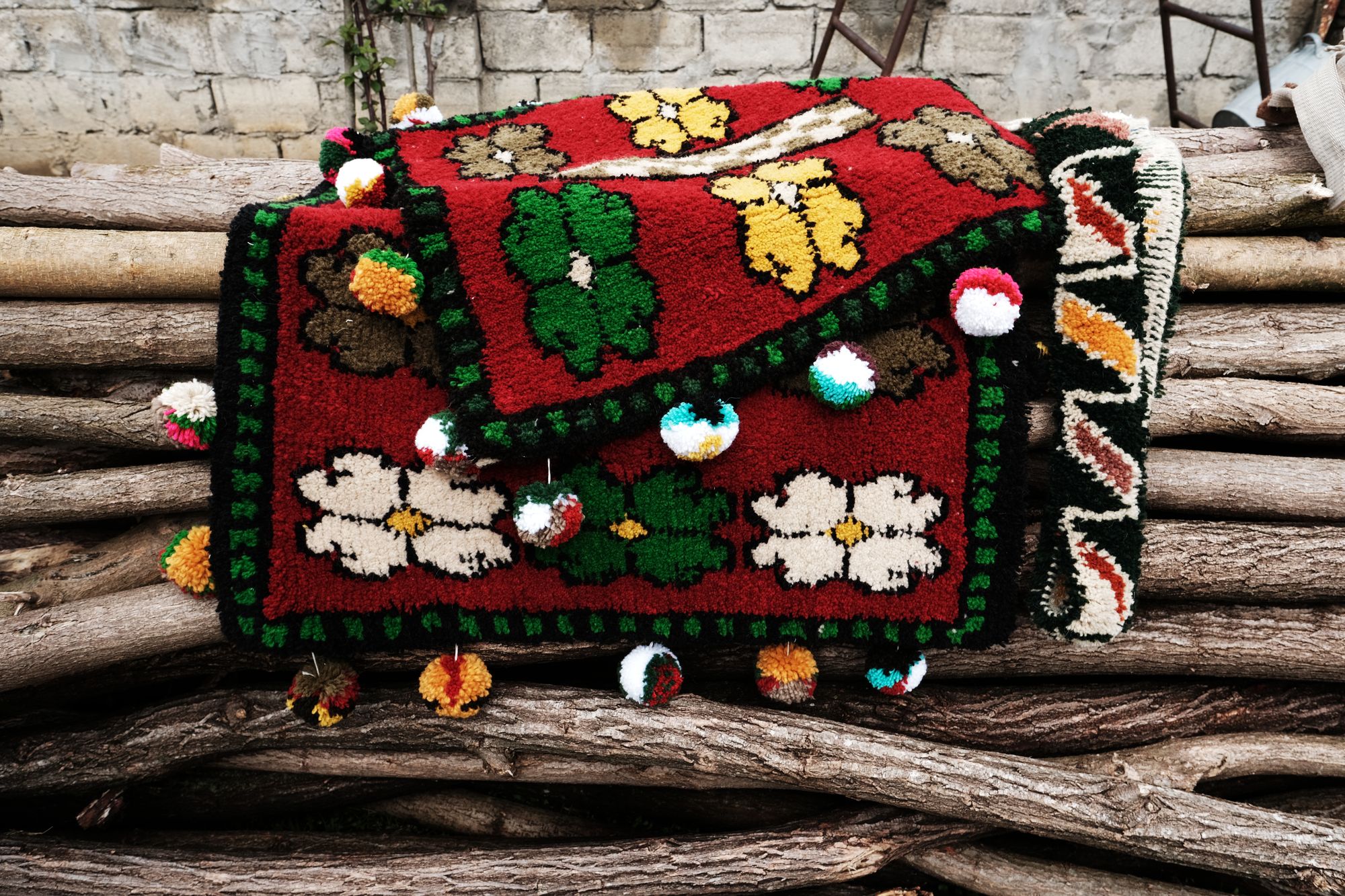 Hand-woven red Shabrak with green and yellow flowers and coloured pompoms draped over weathered logs
