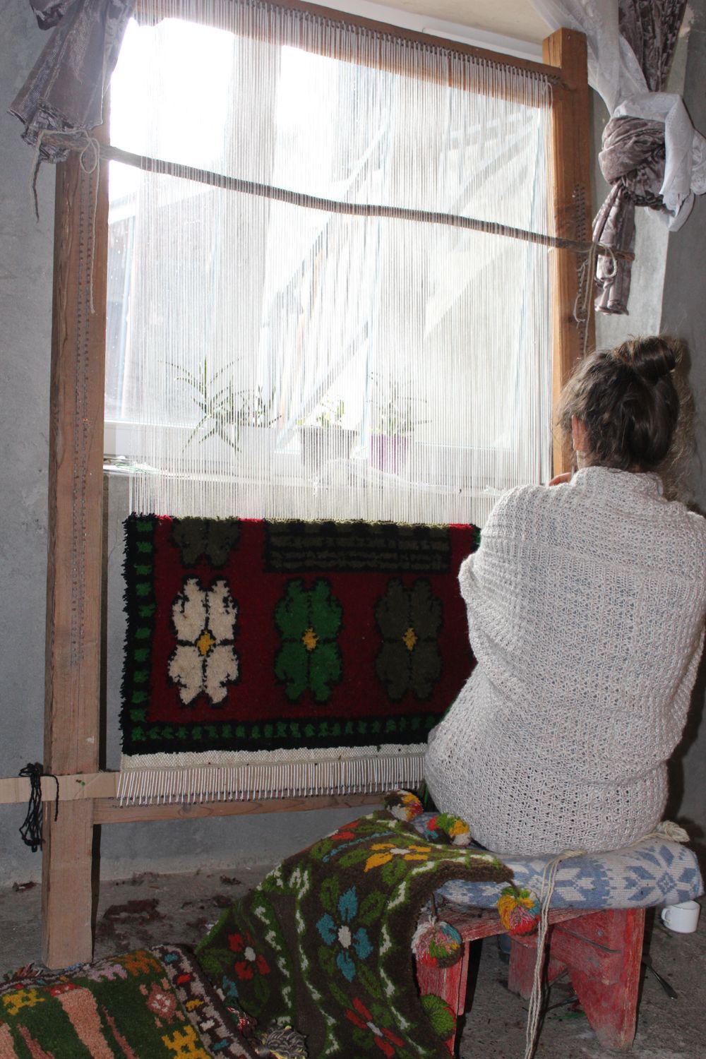 Weaver seated at the loom working a red and green pattern