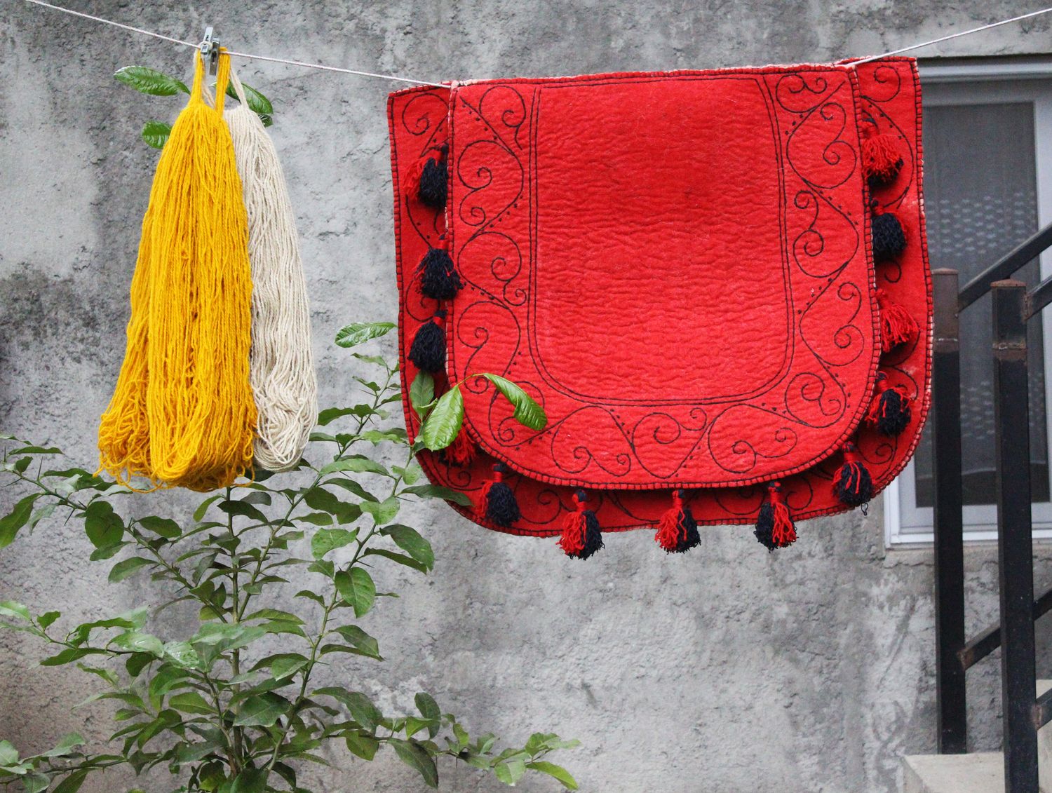 Red felt Shabrak beside hanks of yellow and natural plant-dyed wool