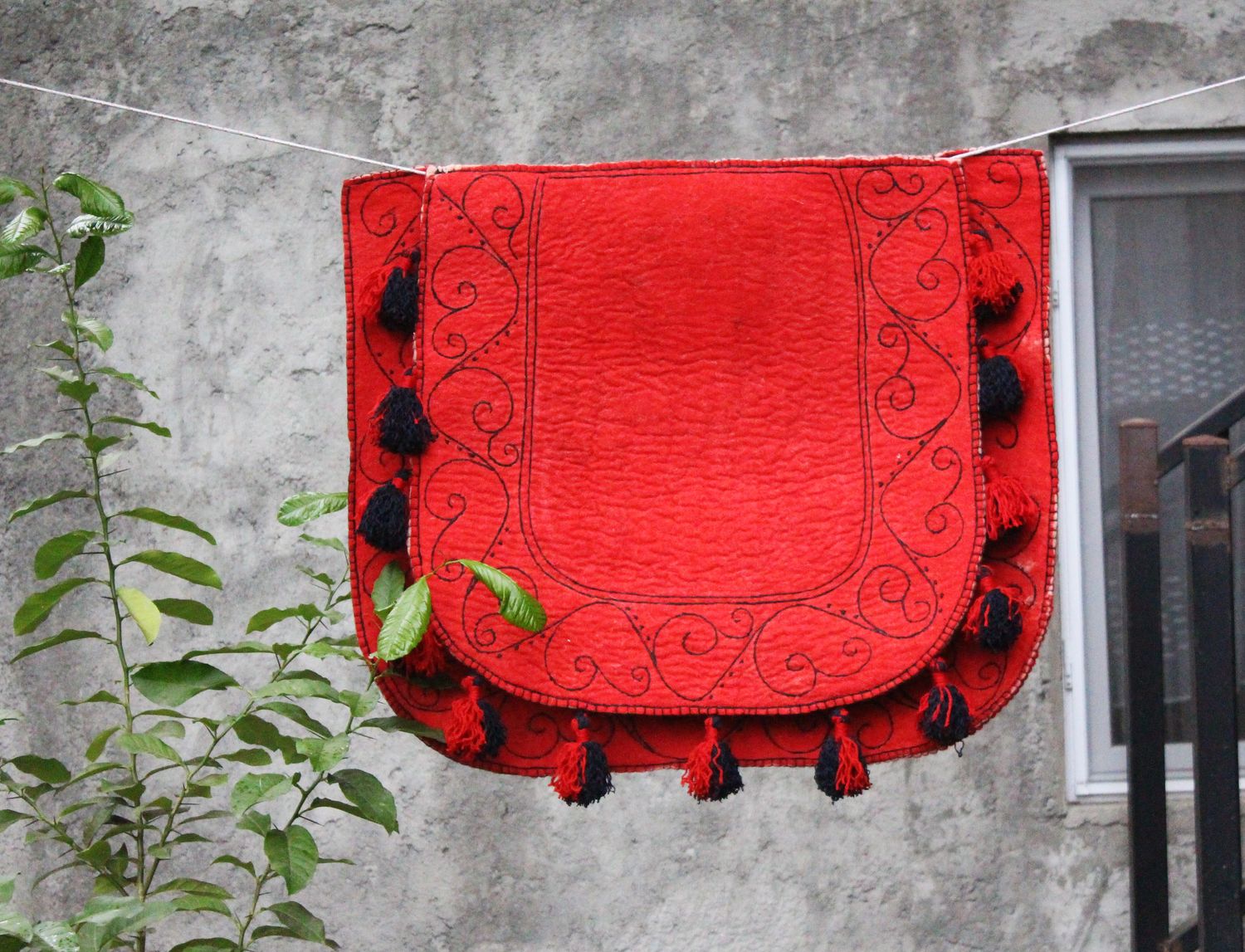 Bright red felt Shabrak with scroll embroidery and black tassels hanging on a wall