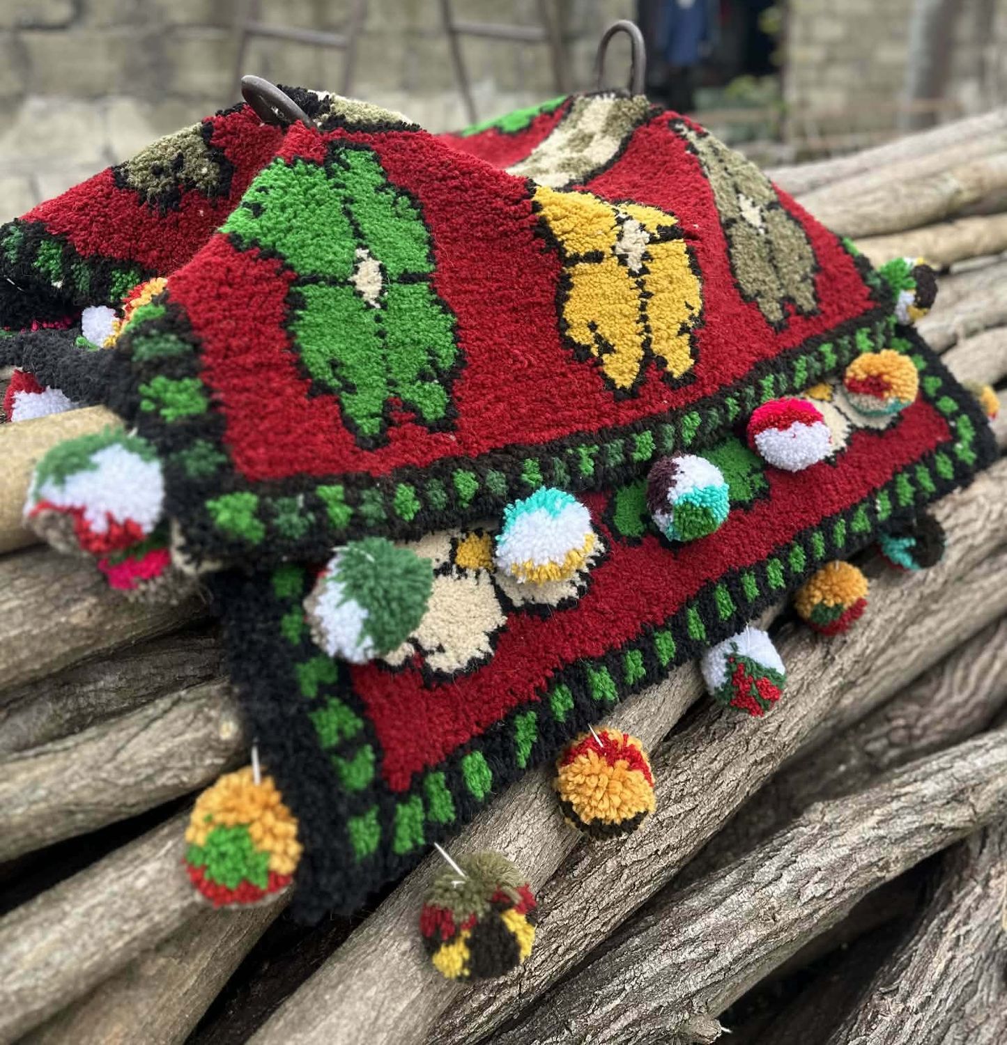 Red woven Shabrak draped over logs with green and cream flowers