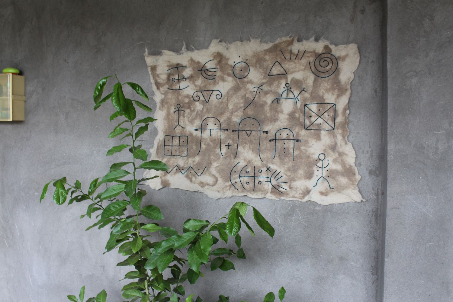 Felt pictogram panel mounted on concrete with a green plant in front