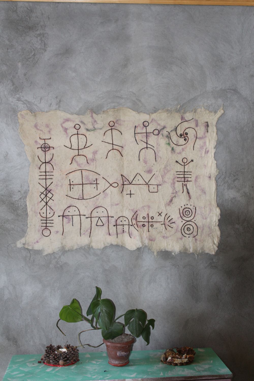 Felt pictogram panel on a grey wall above a shelf with a plant