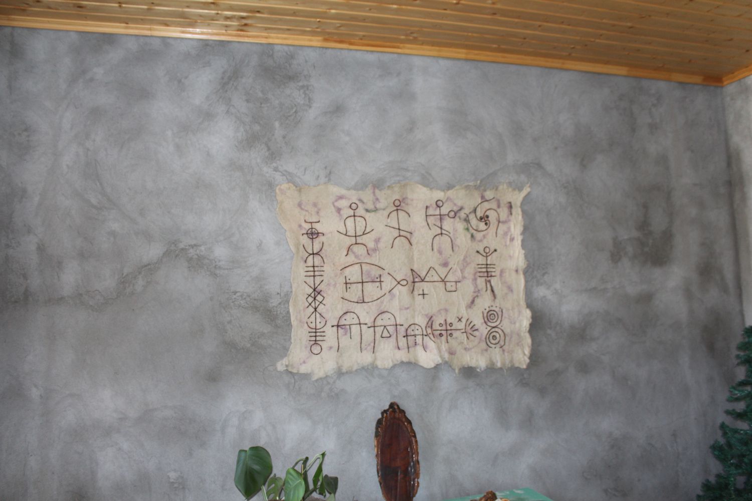 Felt panel with Tushetian pictograms hung on a grey plaster wall