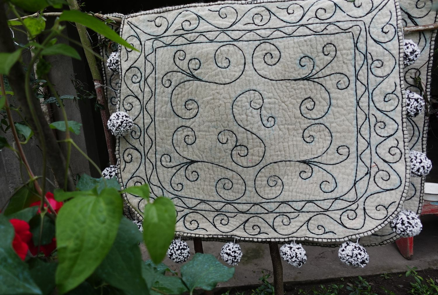 White felt Shabrak with scroll embroidery hanging against foliage